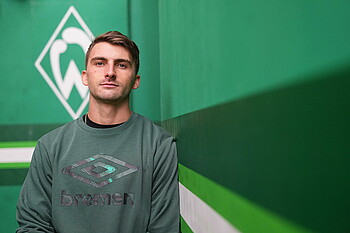 Maximilian Philipp in front of a green wall, in the background is a Werder sign