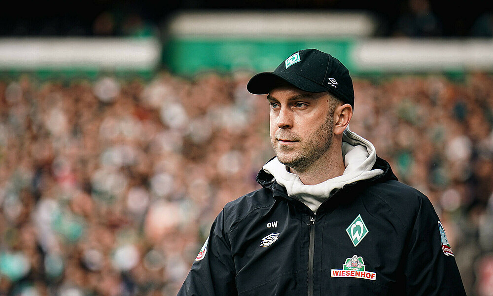 Ole Werner, wearing a Werder cap, looks on from the touchline