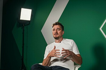 Jahns sitting in front of a green wall for his interview.