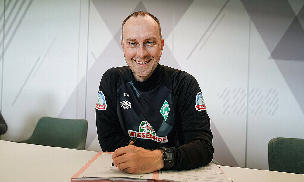 Ole Werner smiling at the camera while he signs the contract.