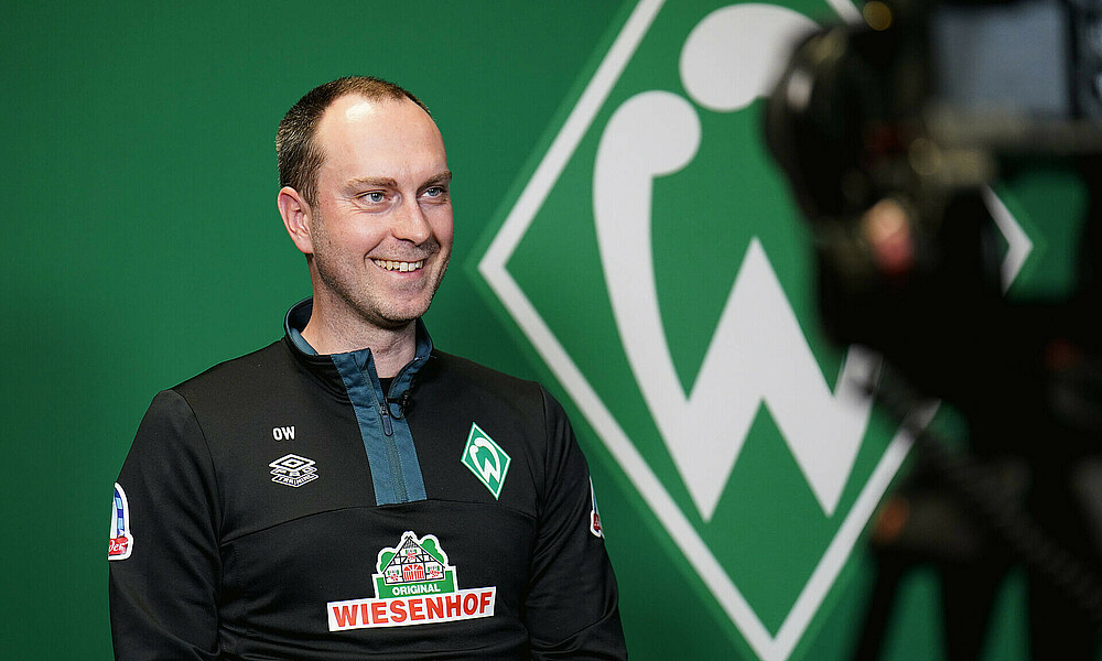 Ole Werner sitting in front of the Werder crest.