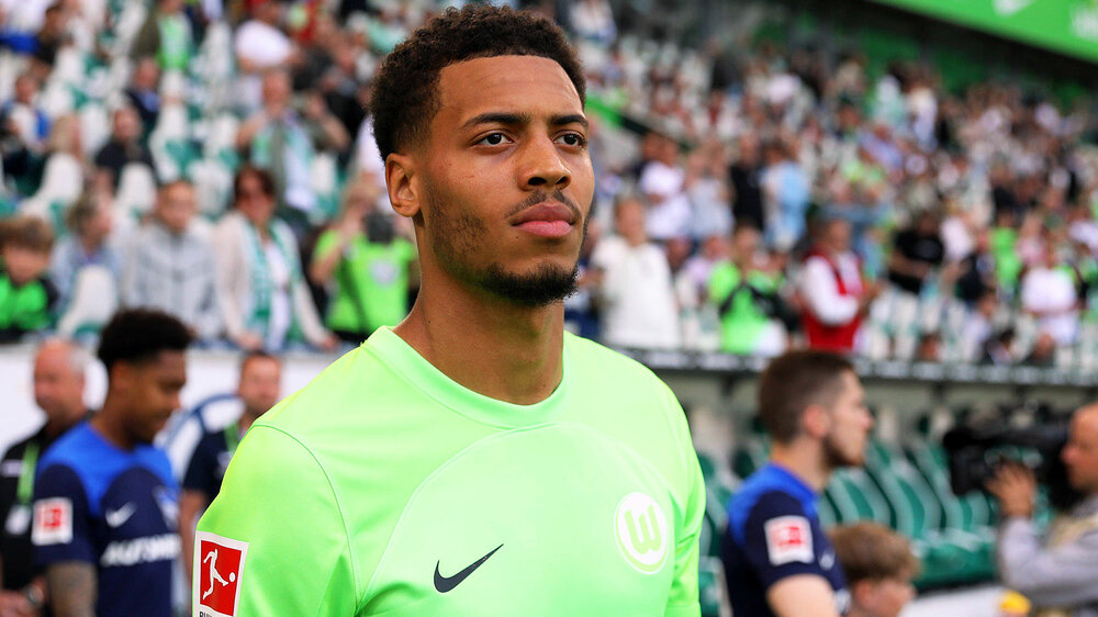 Felix Nmecha vom VfL Wolfsburg schaut mit neutralem Gesichtsausdruck auf das Spielfeld.