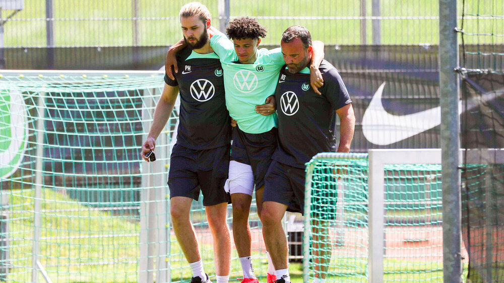 VfL Wolfsburg Spieler Kevin Paredes humpelt, gestützt von zwei Helfern, vom Spielfeld.