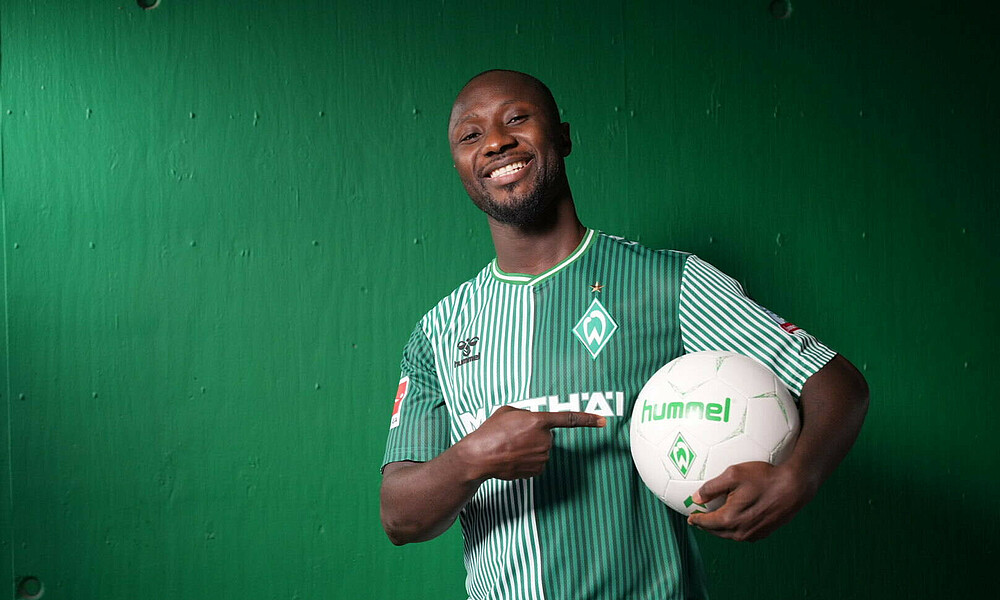 Naby Keïta smiles while holding a football in his hands.