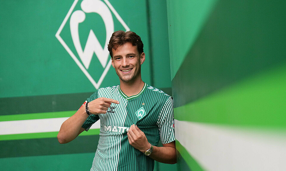 Olivier Deman wearing the Werder home shirt and pointing to the Werder badge.