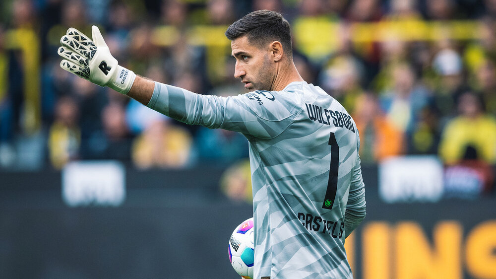 VfL-Wolfsburg-Keeper Koen Casteels hebt einen Arm und hält mit dem anderen einen Ball.