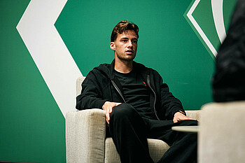 Olivier Deman sitting in an armchair, with a green wall in the background.