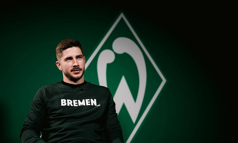 Romano Schmid in a Bremen jumper in front the Werder badge.