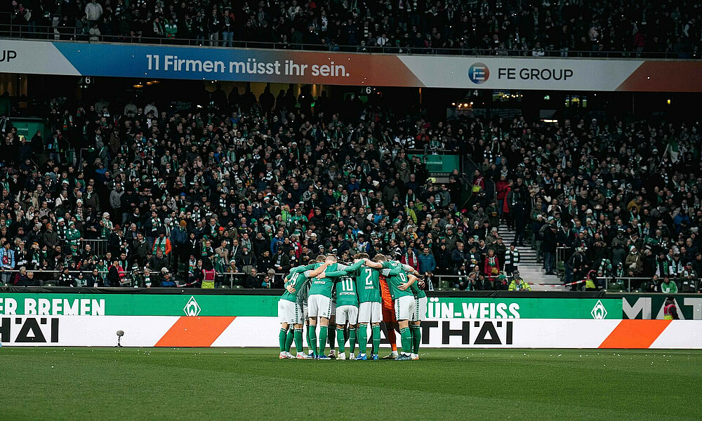 Players in a circle with crowd in the background.