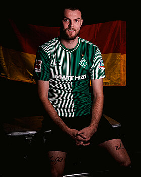 Marvin Ducksch sitting in a Werder top draped in a Germany flag.