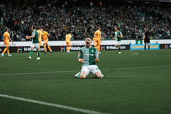 Romano Schmid kneels on the pitch and clenches both fists in celebration.