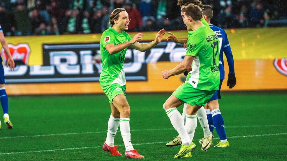 VfL Wolfsburg Spieler Majer läuft auf dem Spielfeld auf Mitspieler Behrens zu und jubelt.