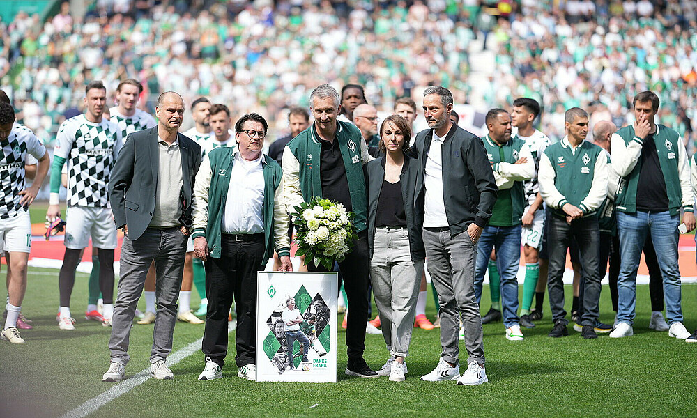 Frank Baumann holding a bouquet of flowers, surrounded by members of the club's executive team. In the background are members of the current squad, as well as our 2004 double-winning side.