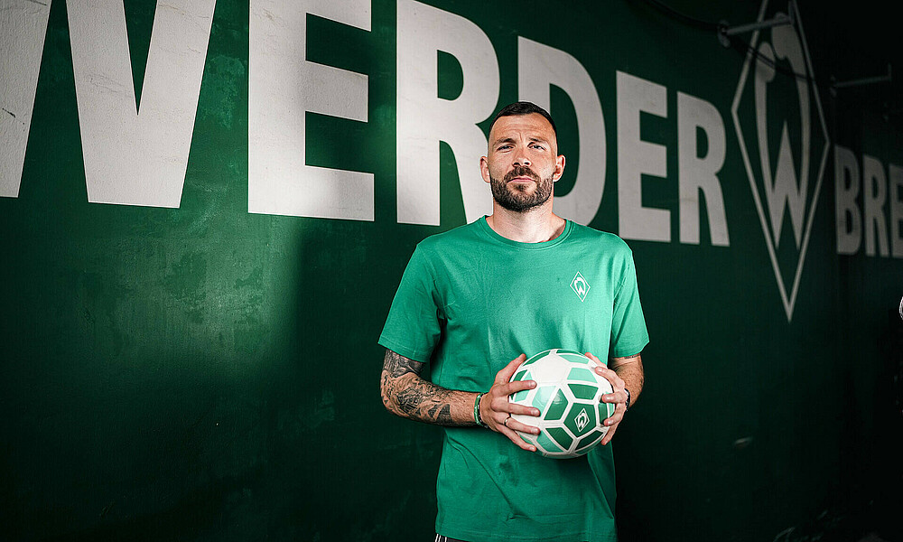 Kolke with a ball in his hand in front of a Werder-style wall.