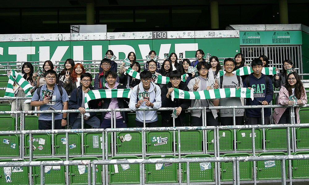 A class of Vietnamese pupils stand in the Ostkurve holding SVW scarves.