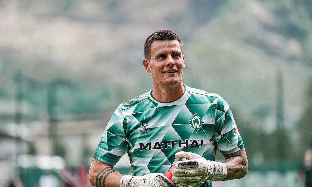 Michael Zetterer looks upwards. He is wearing the green and white warm-up kit. He's also wearing goalkeeper gloves and carrying a drinks bottle.