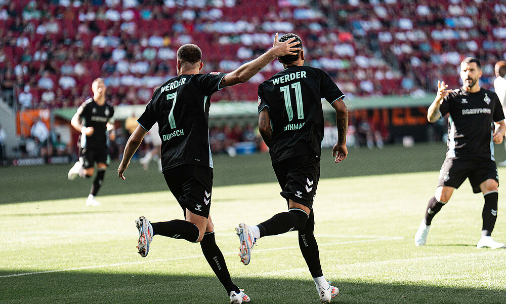 A photo of Marvin Ducksch and Justin Njinmah running from behind. Marvin Ducksch has his hand on Justin Njinmah's head. hat die Hand auf dem Kopf von Justin Njinmah.