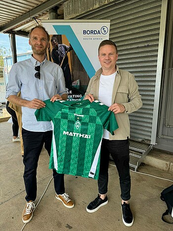 Two people hold up a Werder jersey.