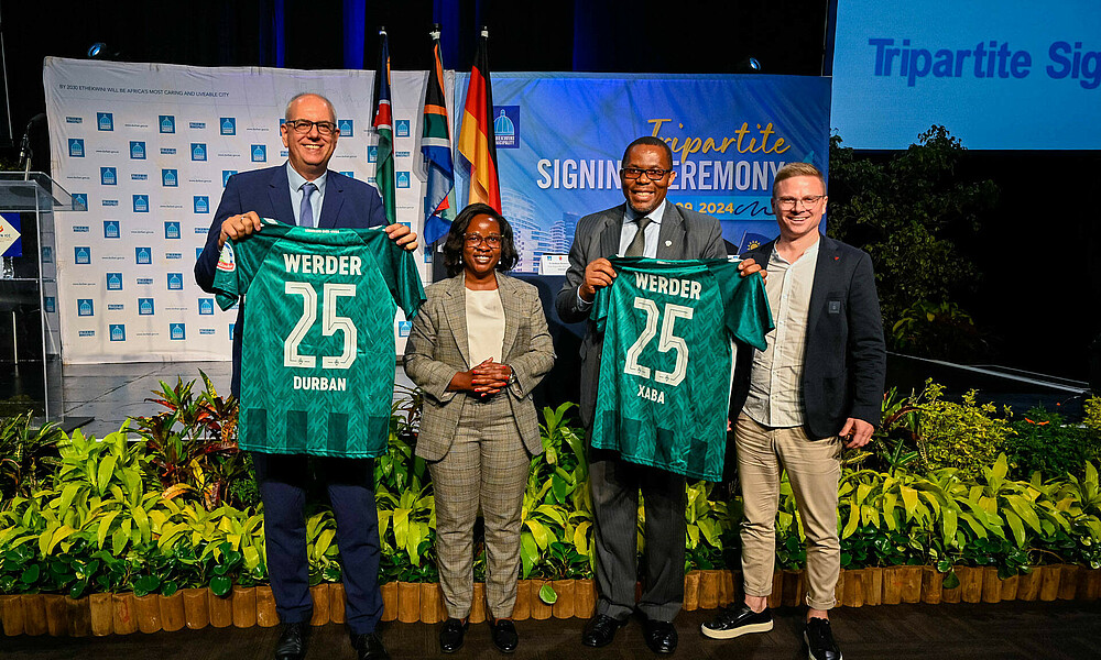 Multiple people pose together for a photo, holding up Werder kits.